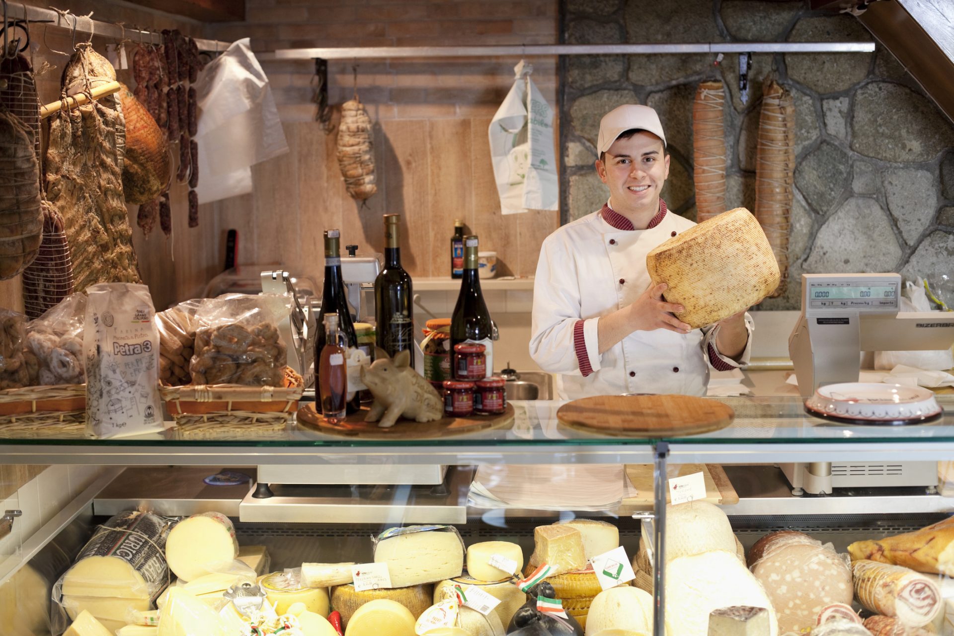 young man working at delicatessen, holding cheese